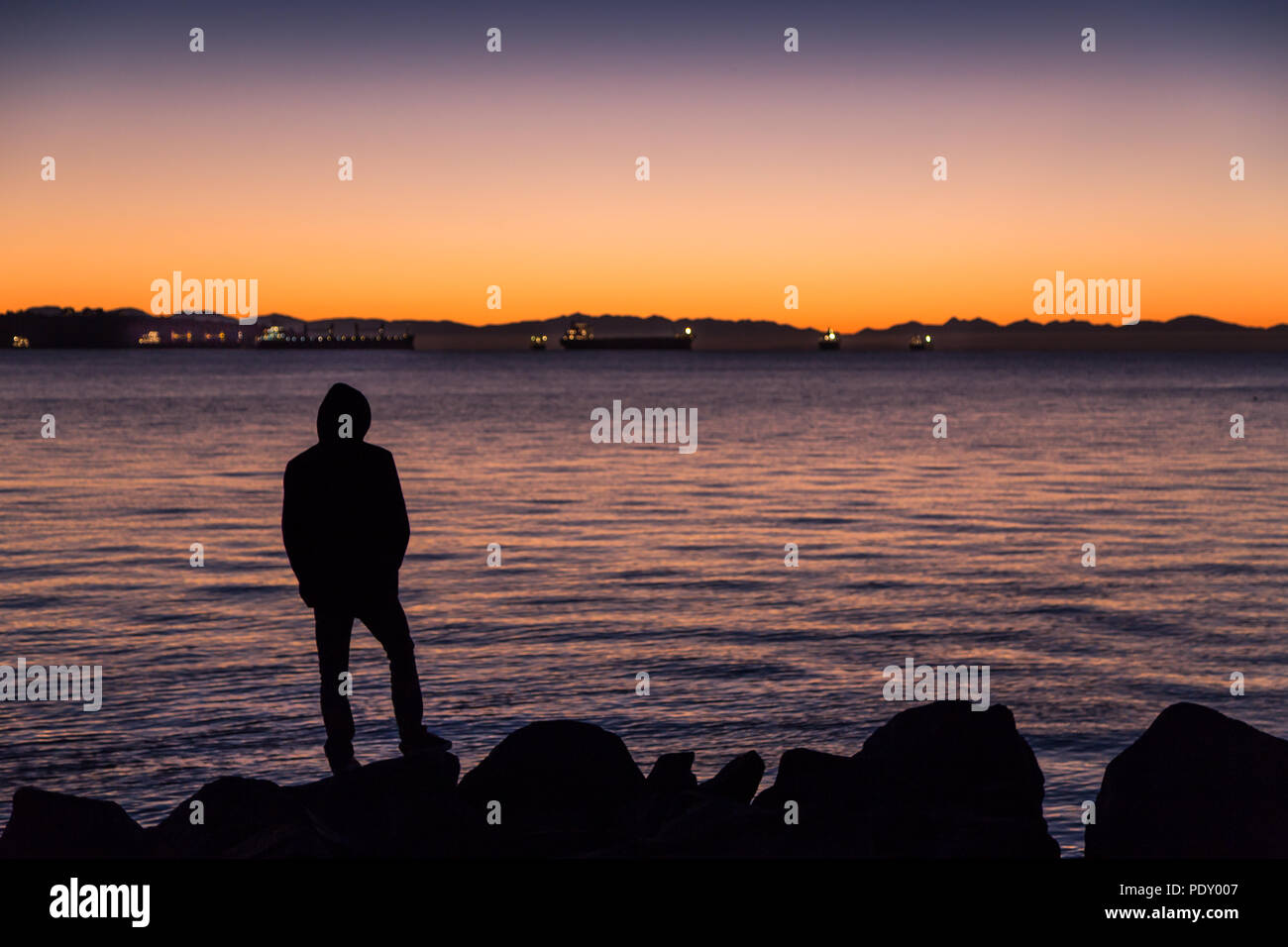 Hombre de pie junto al océano, mirando hacia el horizonte. Foto de stock