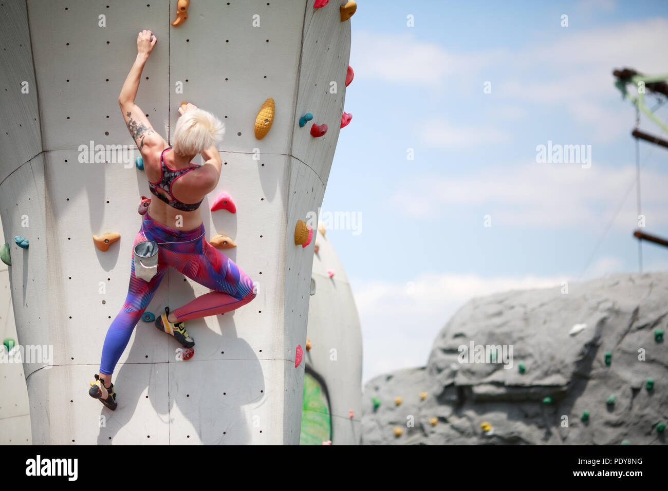 de la de atrás del deporte mujer con pelo corto en ropa deportiva en entrenar en pared para escalar en roca contra el azul con nubes en la tarde