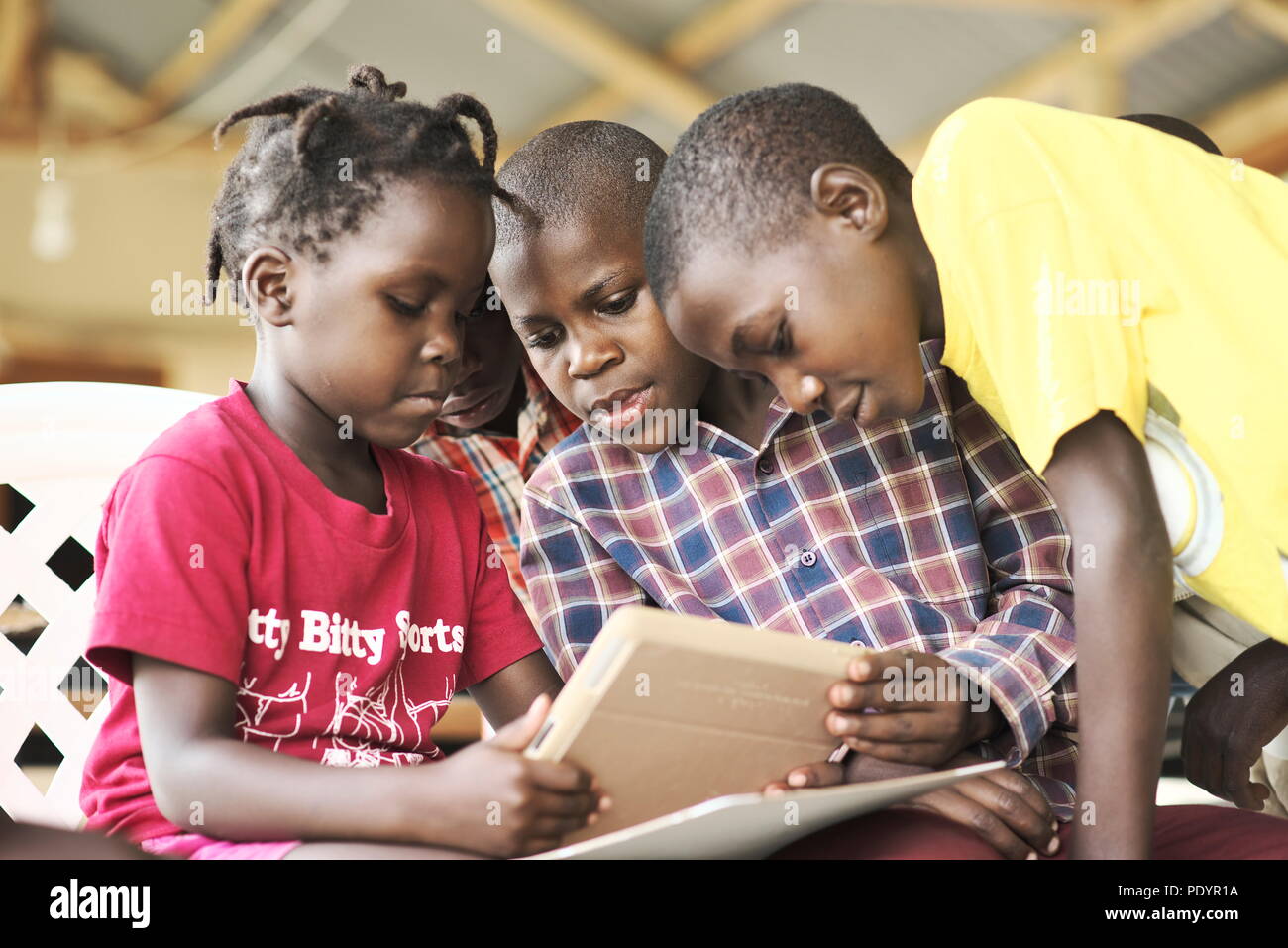 Un grupo de niños ugandeses jóvenes se reúnen en un grupo usando ropa brillante para usar UN IPAD de Apple por primera vez Foto de stock