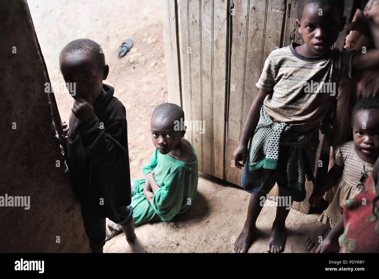 Un joven niño ugandés que es VIH-positiva se sienta en la puerta de su casa, mirando a la cámara con sus hermanos Foto de stock