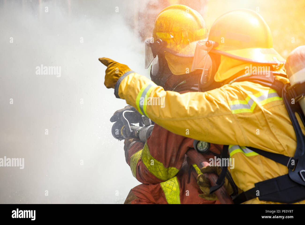 La acción de cierre de dos bomberos de pulverización de agua de alta presión por la boquilla al fuego rodean por el humo con brillos y espacio de copia Foto de stock