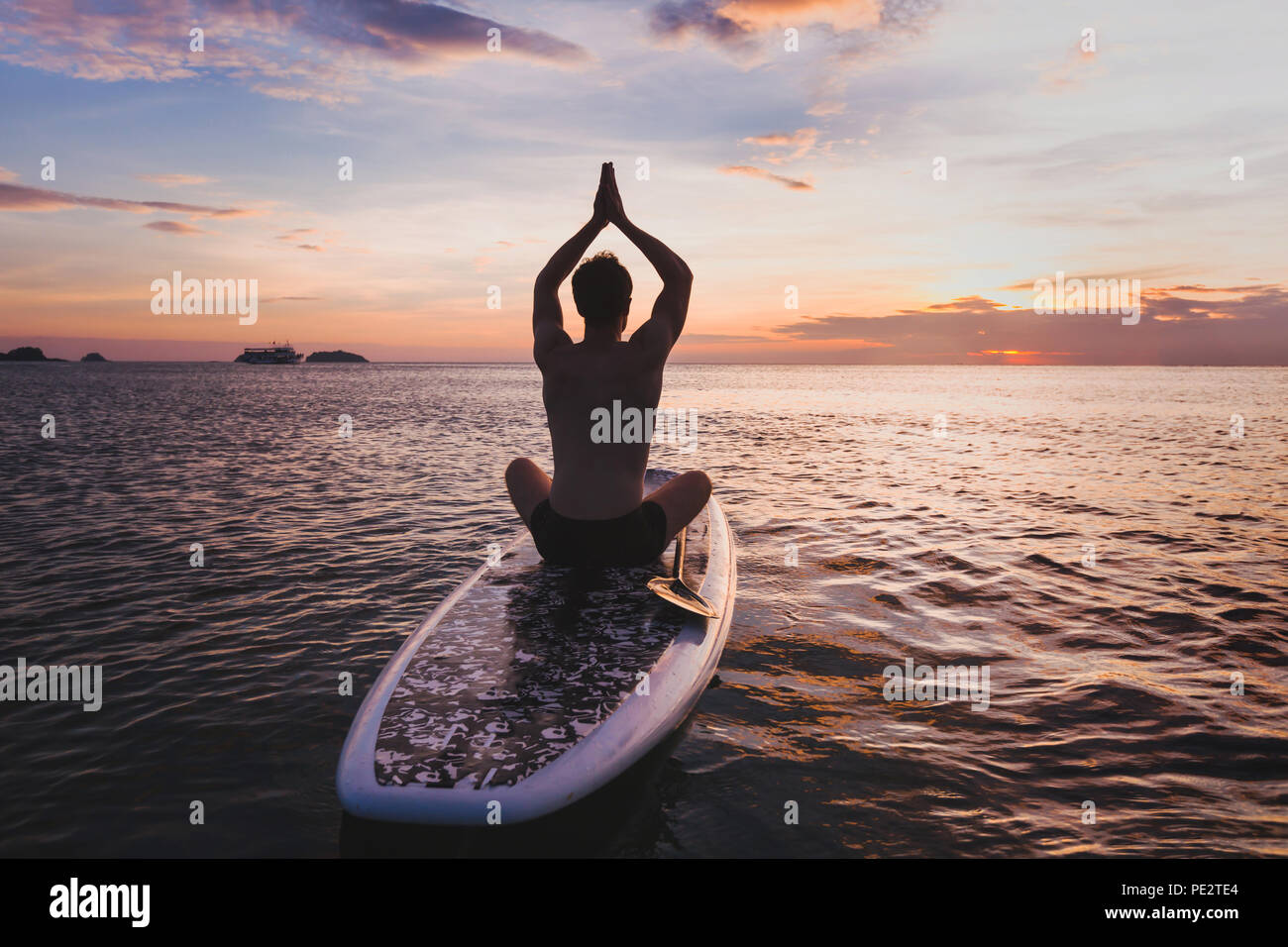 Yoga en SUP, la silueta del hombre sentado en la postura del loto en el stand up paddle board Foto de stock