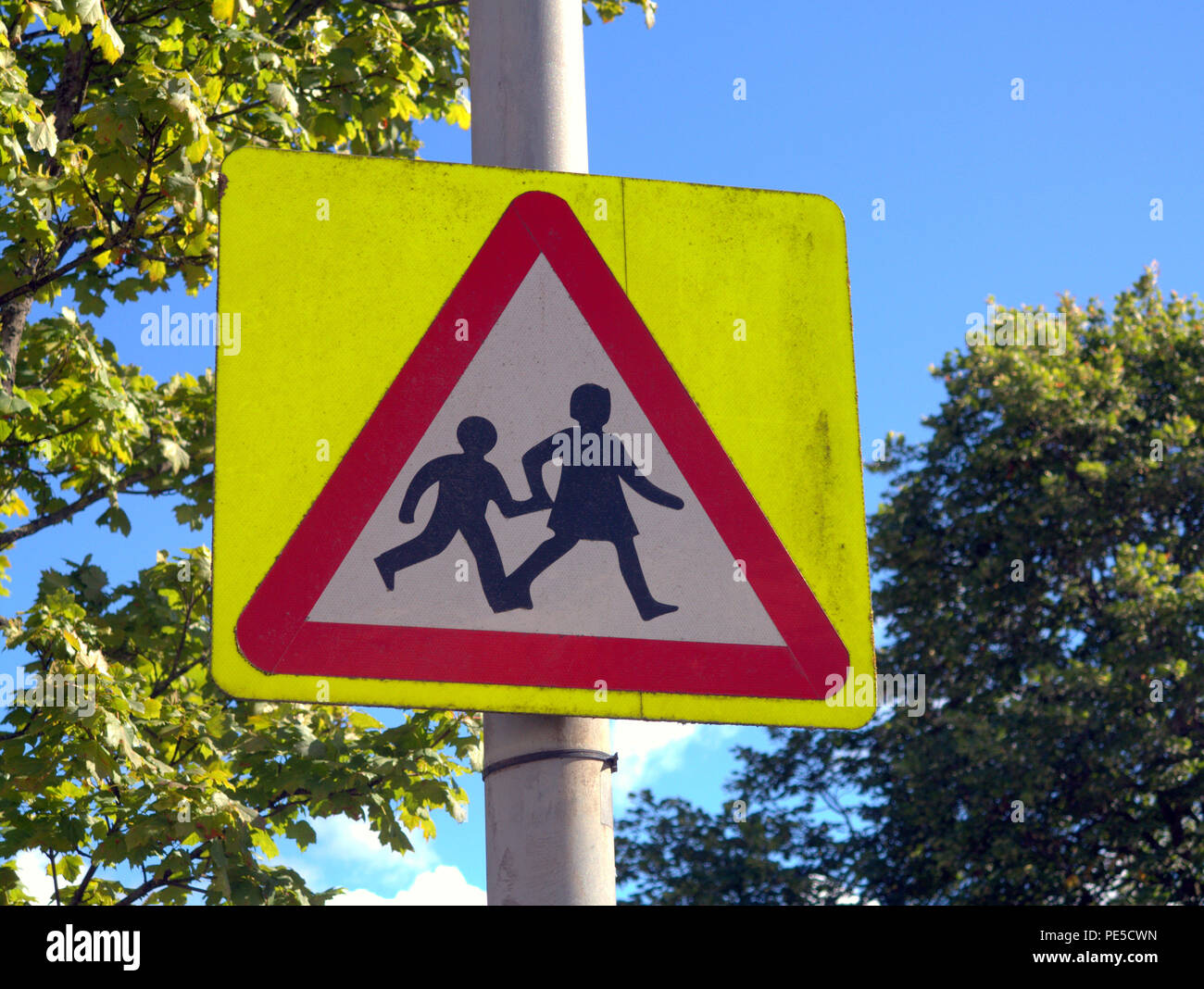 Señal de carretera británica escolares los niños crossing road signo de advertencia de cielo azul Foto de stock
