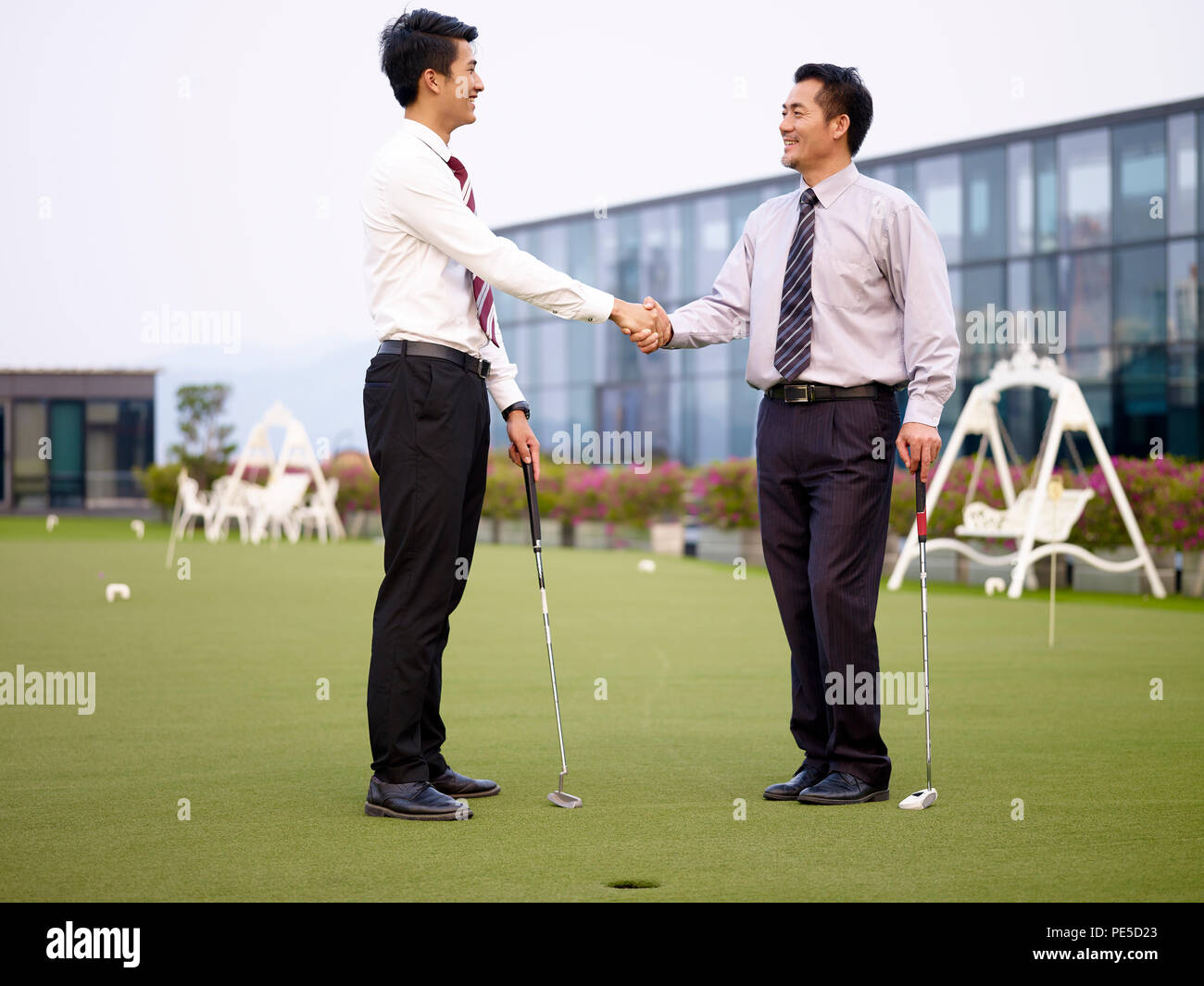 Dos ejecutivos de empresas asiáticas agitando las manos después de jugar al golf en la azotea corte. Foto de stock