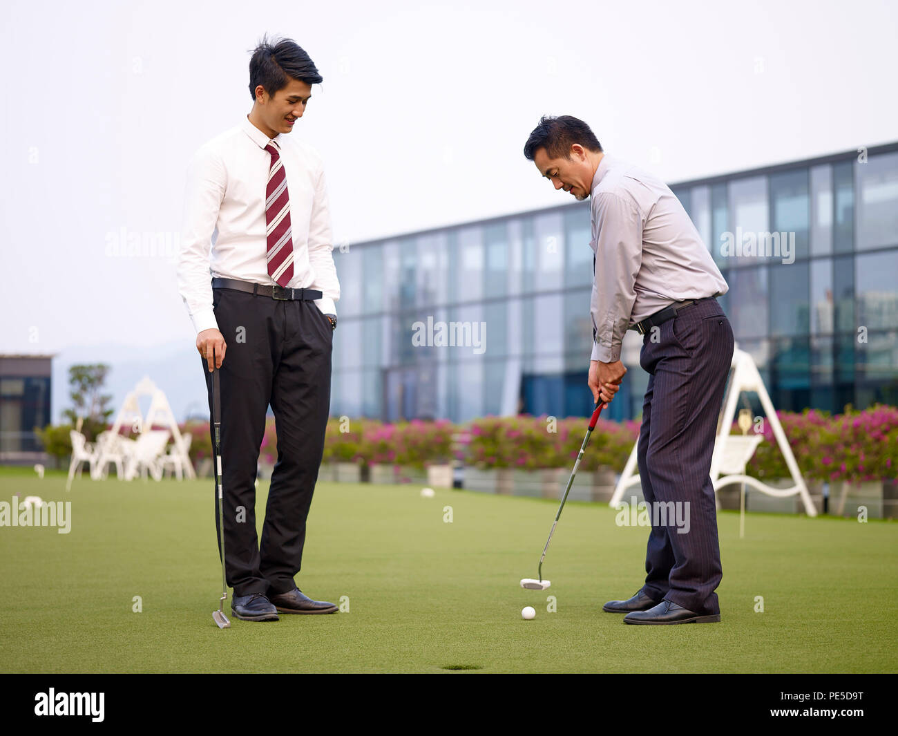 Dos hombres de negocios asiáticos relajarse y jugar al golf en la azotea corte. Foto de stock