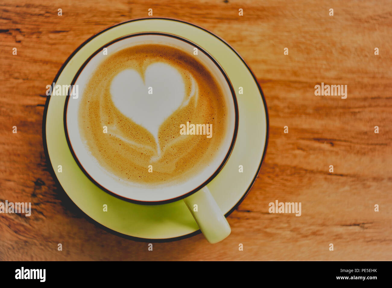 Cappuccino café caliente con forma de corazón de espuma en el fondo de la tabla de madera Foto de stock
