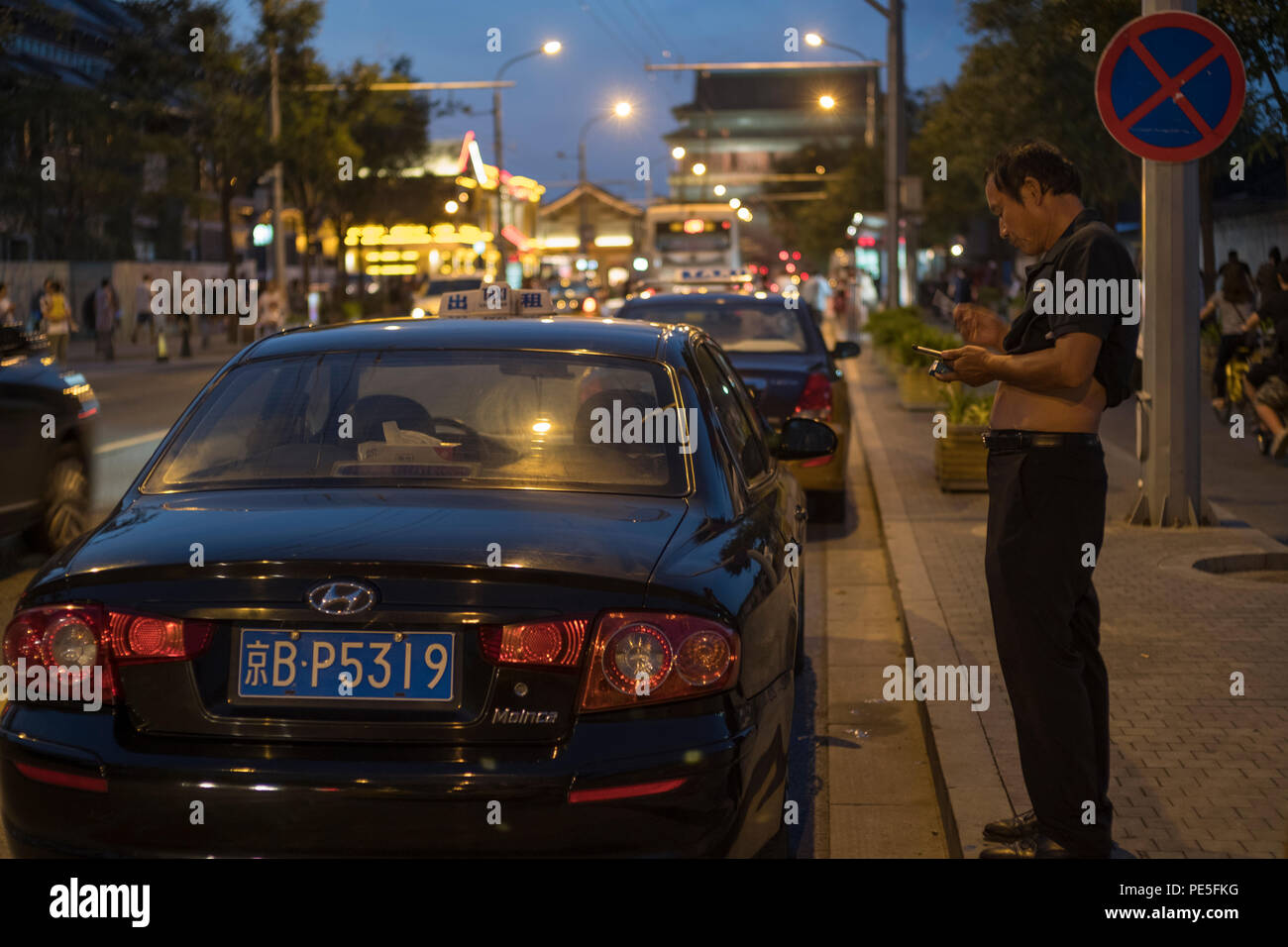 Un taxista que utiliza un teléfono móvil mientras espera a los clientes fuera de una estación de metro en Beijing, China. 08-ago-2018 Foto de stock