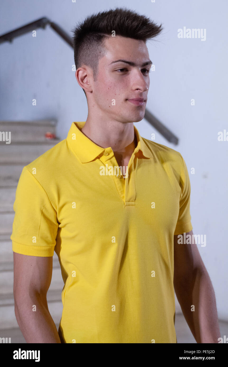 Cabello castaño joven modelo masculino con camisa de polo amarillo, de moda joven muchacho serio con hombres de color amarillo del cuello de Polo T-Shirt Foto de stock