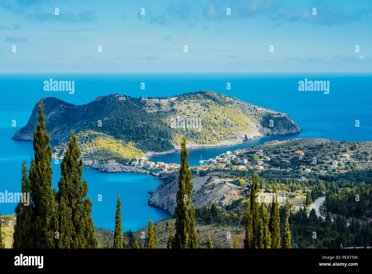 Vista anterior a Assos Village y el hermoso mar azul. Cipreses destaca en primer plano. La isla de Cefalonia, Grecia Foto de stock