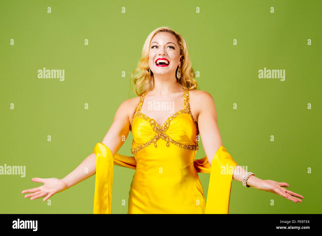 Disfrutando el protagonismo, un elegante rubia con los brazos, aislado sobre fondo verde studio Foto de stock