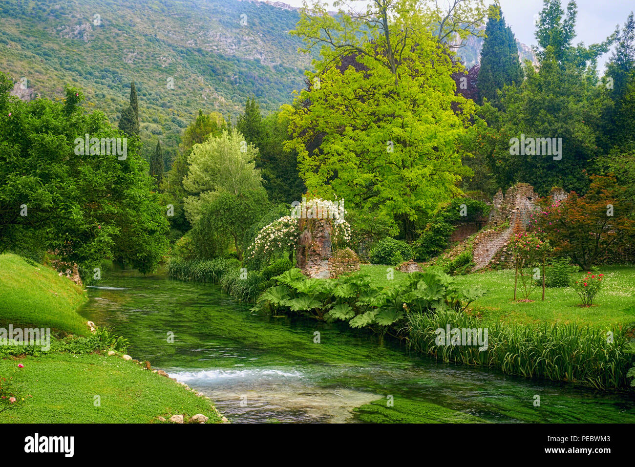 Un exuberante jardín con un riachuelo y ruinas históricas, Ninfa Jardín, Cisterna di Latina, Italia Foto de stock