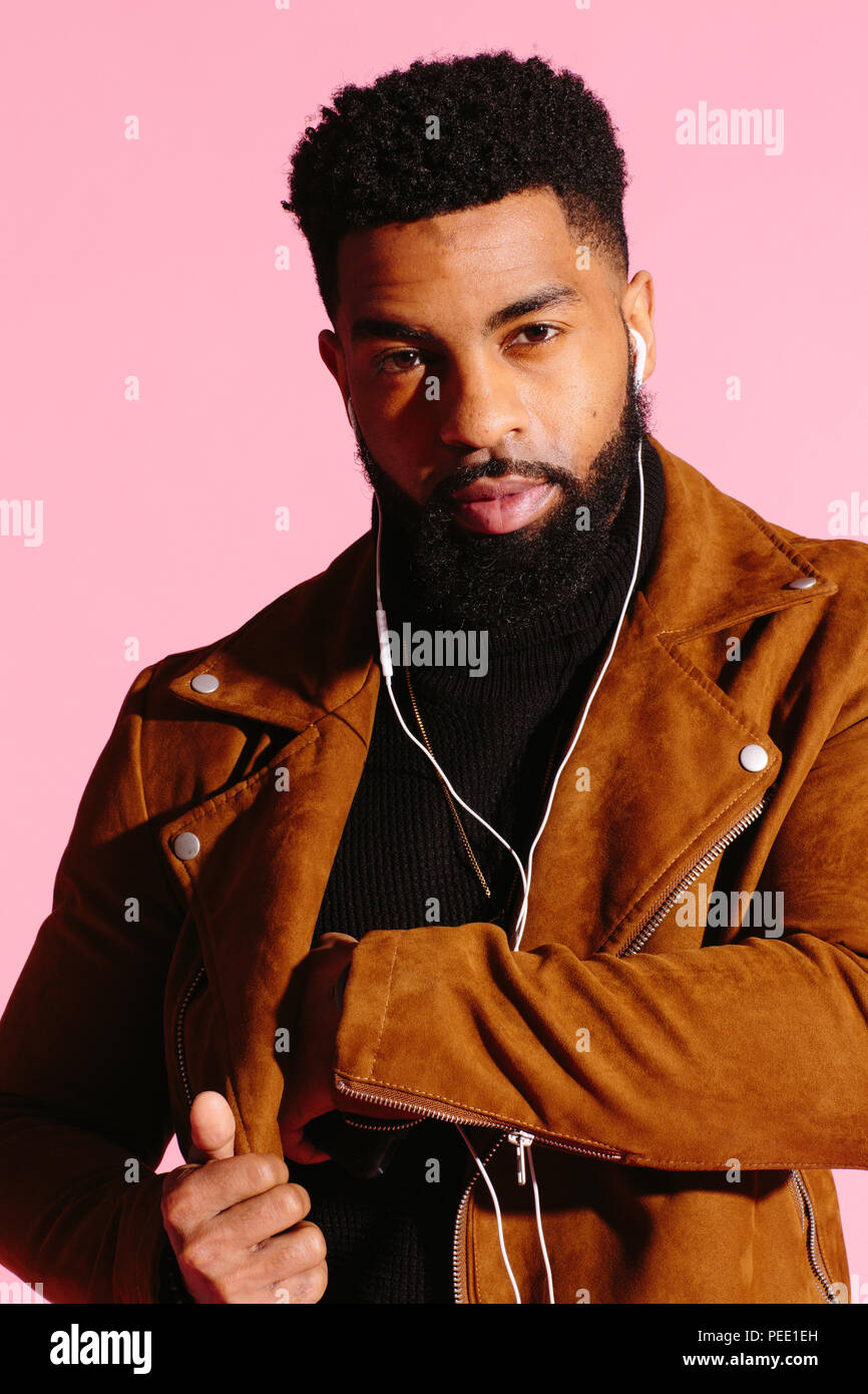 Cool hombre afroamericano con barba, escuchando música, mirando a la cámara, aislado sobre fondo rosa studio Foto de stock