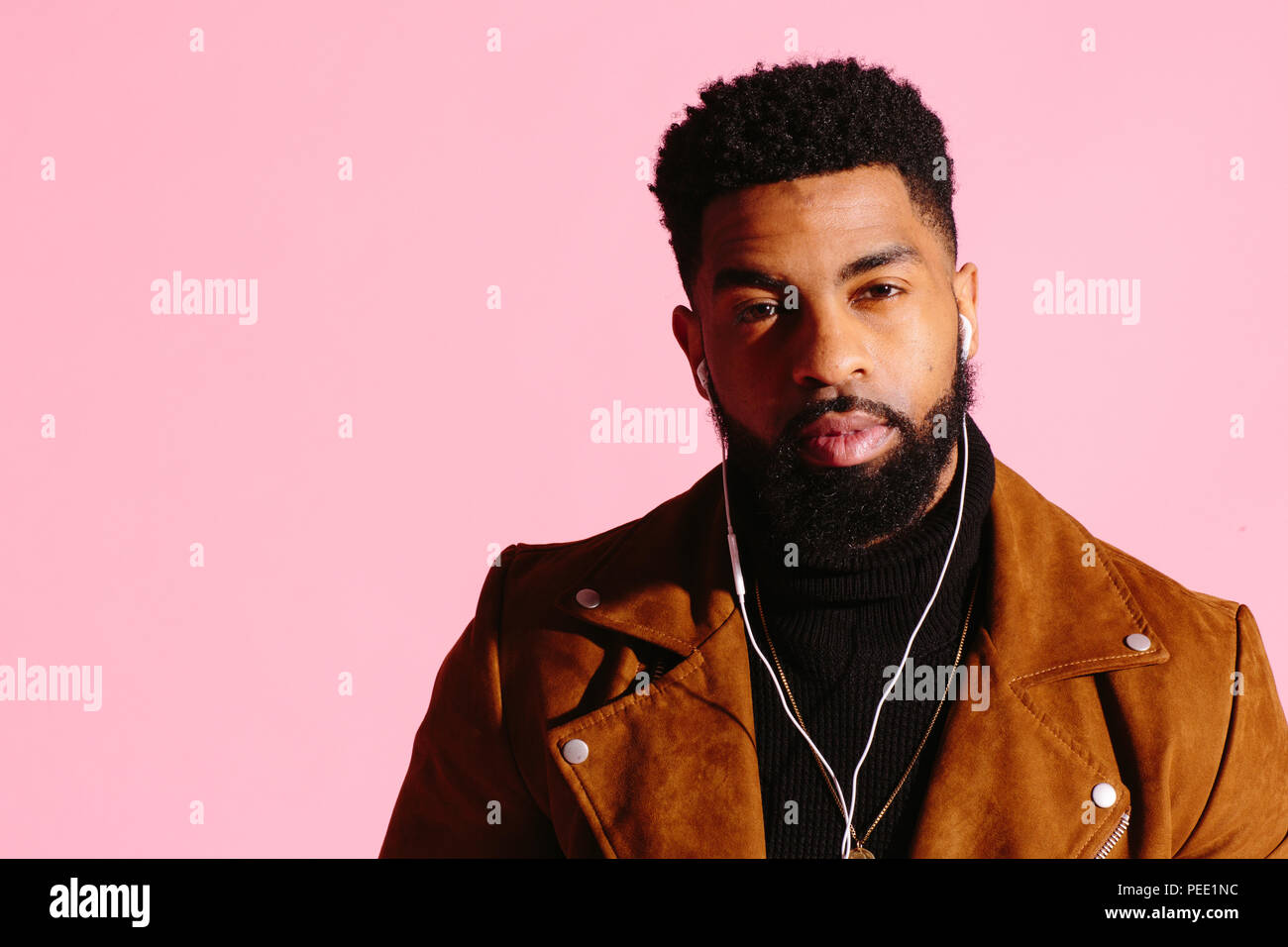 Guapo y cool hombre afroamericano con barba, escuchando música, mirando a la cámara, aislado sobre fondo rosa studio Foto de stock