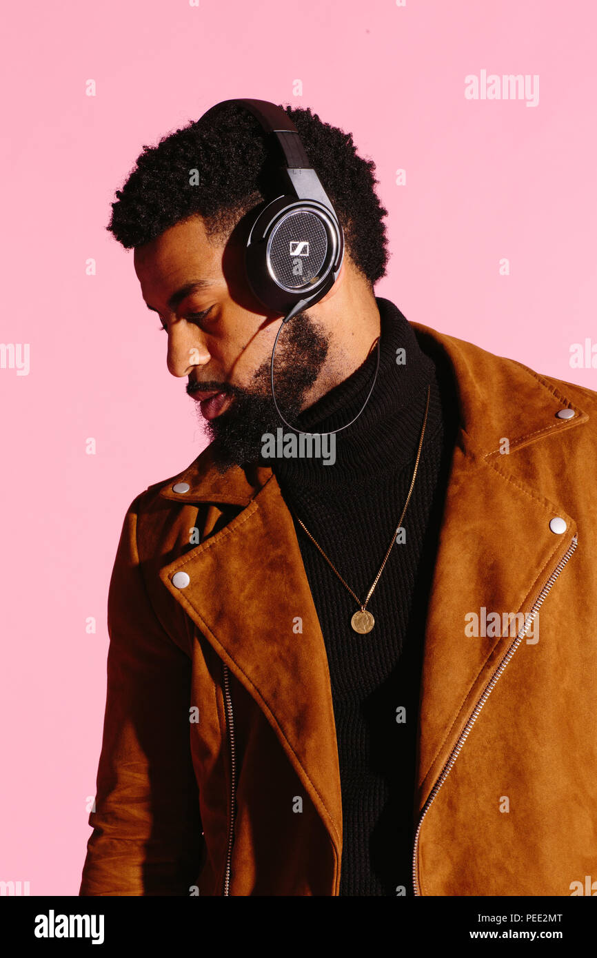 Elegante, guapo y cool hombre afroamericano con barba, escuchando música, aislado sobre fondo rosa studio Foto de stock