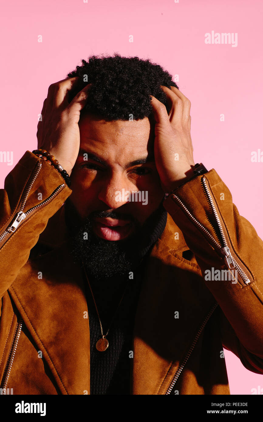 Elegante, guapo y cool hombre afroamericano con barba, aislado sobre fondo rosa studio Foto de stock