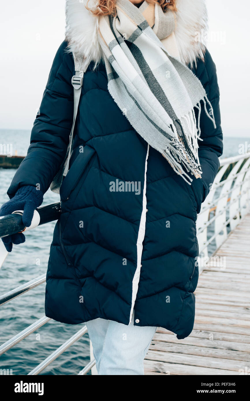 Caminar en temporada de frío en la ropa de abrigo. Joven mujer vistiendo  Down Jacket, capucha, guantes tejidos cálidos y bufanda de pie en el paseo  de invierno contra el Fotografía de