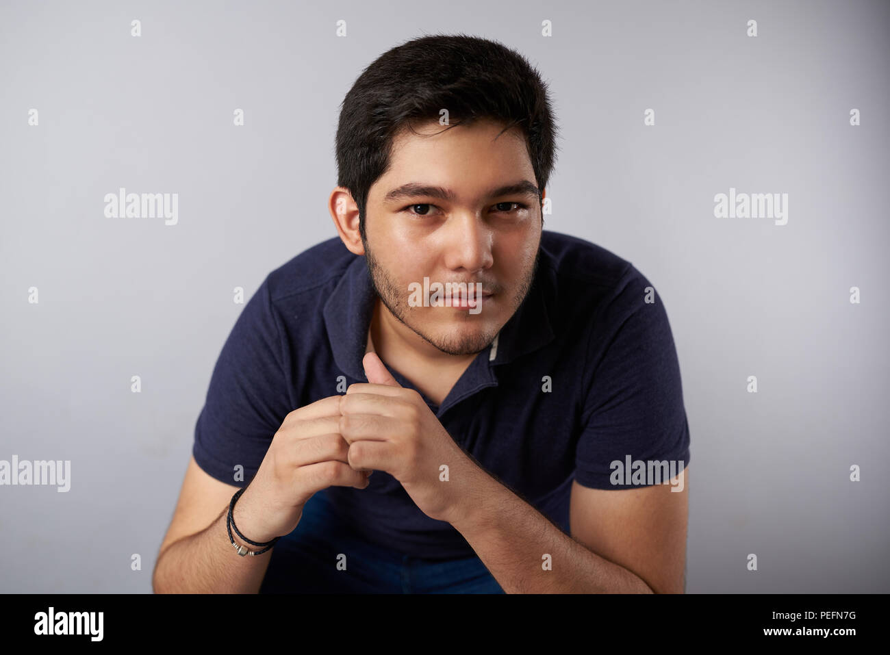 Adolescente hispano hombre retrato sobre fondo gris de studio con manos juntas Foto de stock