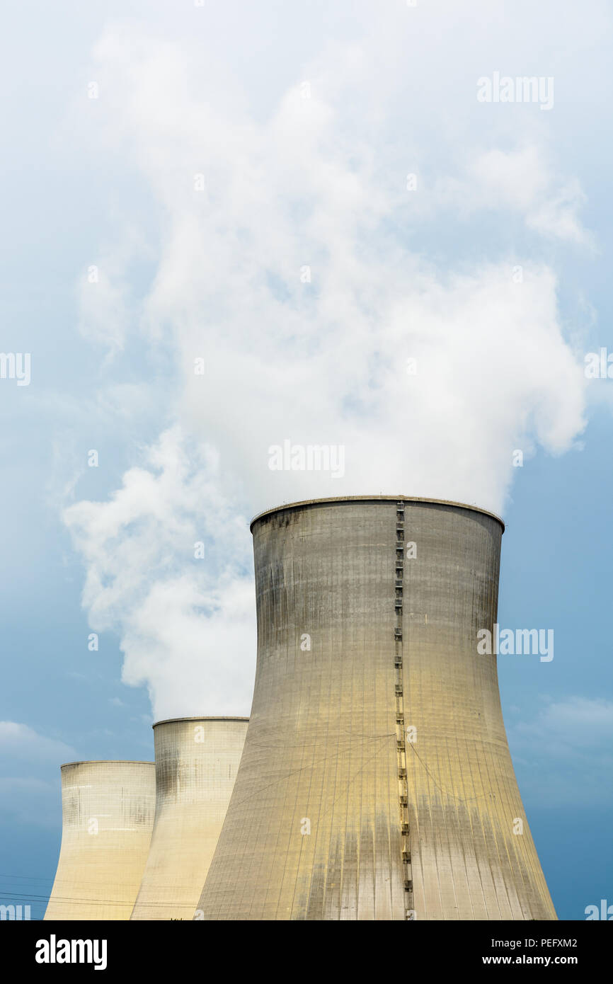 Tres torres de refrigeración de tiro natural de una planta de energía nuclear libera nubes de vapor de agua contra un oscuro cielo tormentoso. Foto de stock