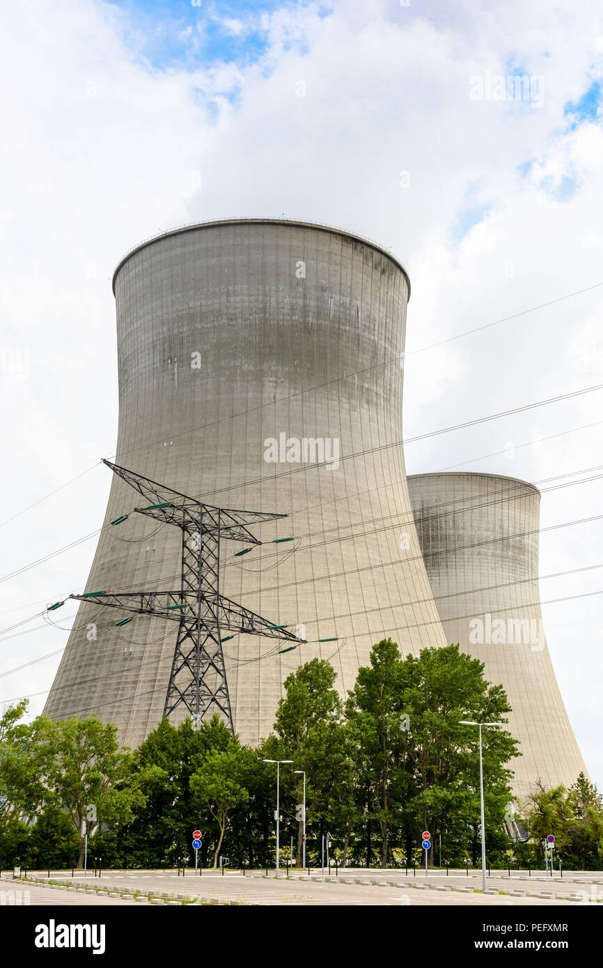 Dos torres de refrigeración de una planta de energía nuclear libera nubes de vapor de agua con una torre de transmisión y un estacionamiento en el primer plano. Foto de stock