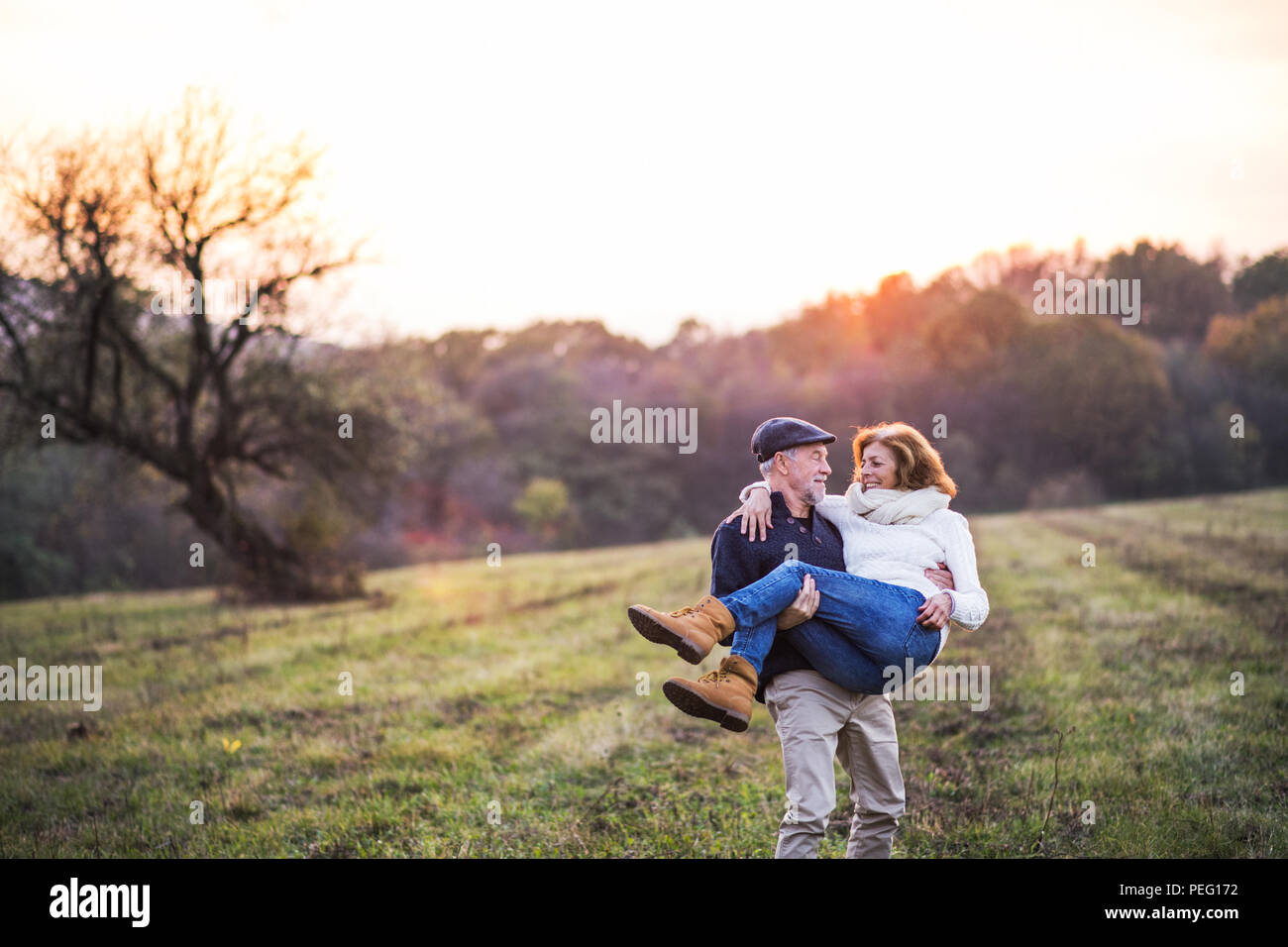 Altos hombre llevando a una mujer en sus brazos en un otoño naturaleza al atardecer. Foto de stock