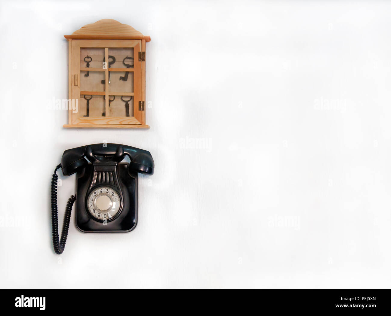 Teléfono antiguo negro y almacenamiento de madera con diferentes claves sobre la pared blanca Foto de stock