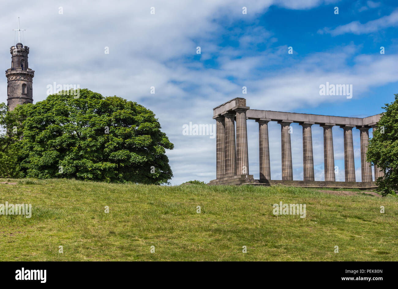 Edimburgo, Escocia, Reino Unido - 13 de junio de 2012: Nelson y Monumentos Nacionales sobre Calton Hill capturados entre el verde de los árboles detrás de césped verde y azul bajo cl Foto de stock