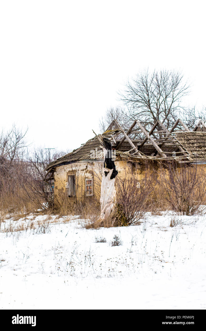 Antigua casa de arcilla en la aldea ucraniana. Ruinas de la casa de barro  en la nieve. Las ruinas de la casa de arcilla seca y los árboles Fotografía  de stock -