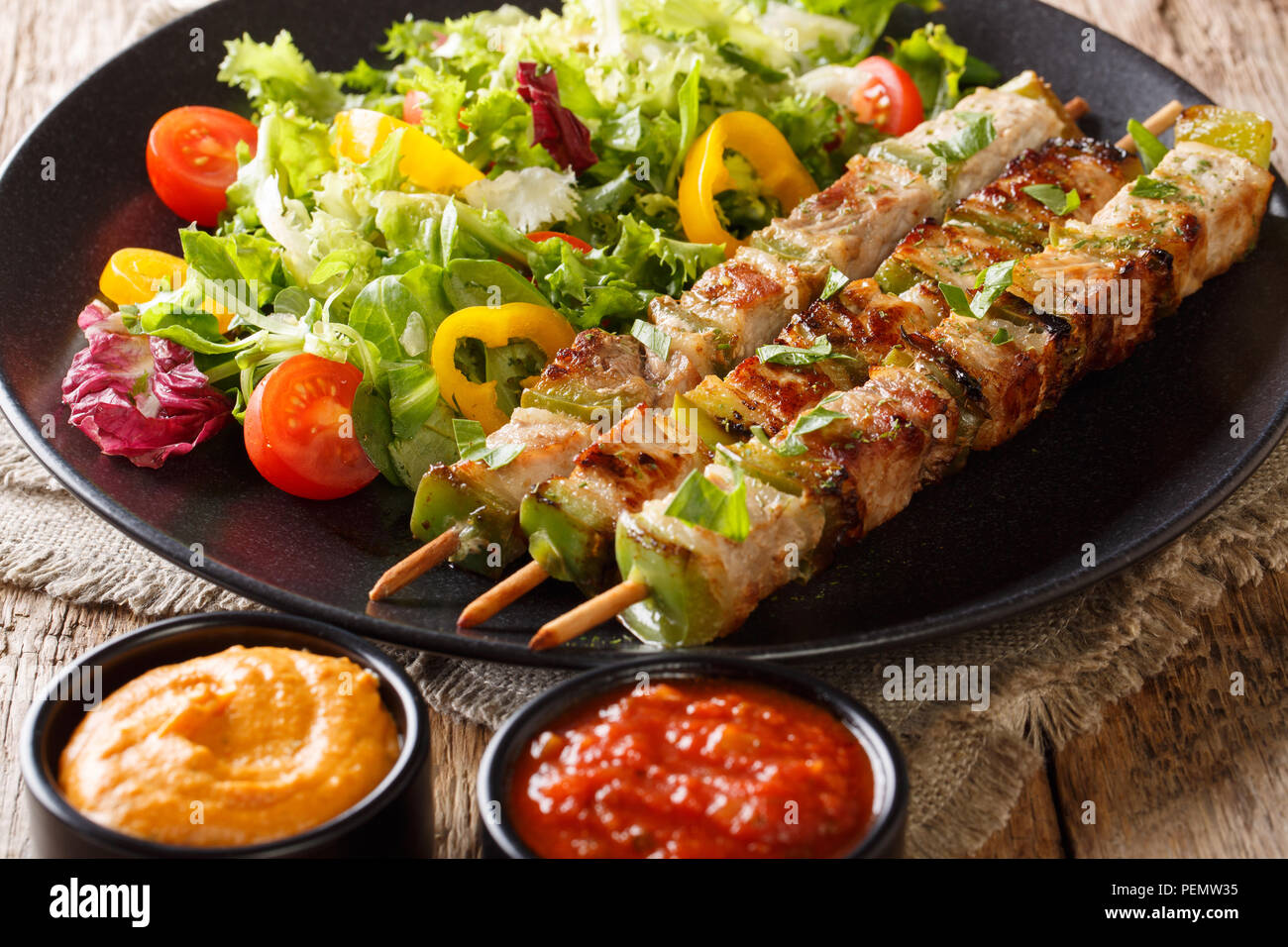 Grill kebab con verduras en brochetas con ensalada fresca en un plato y las salsas de cerca en una mesa horizontal. Foto de stock