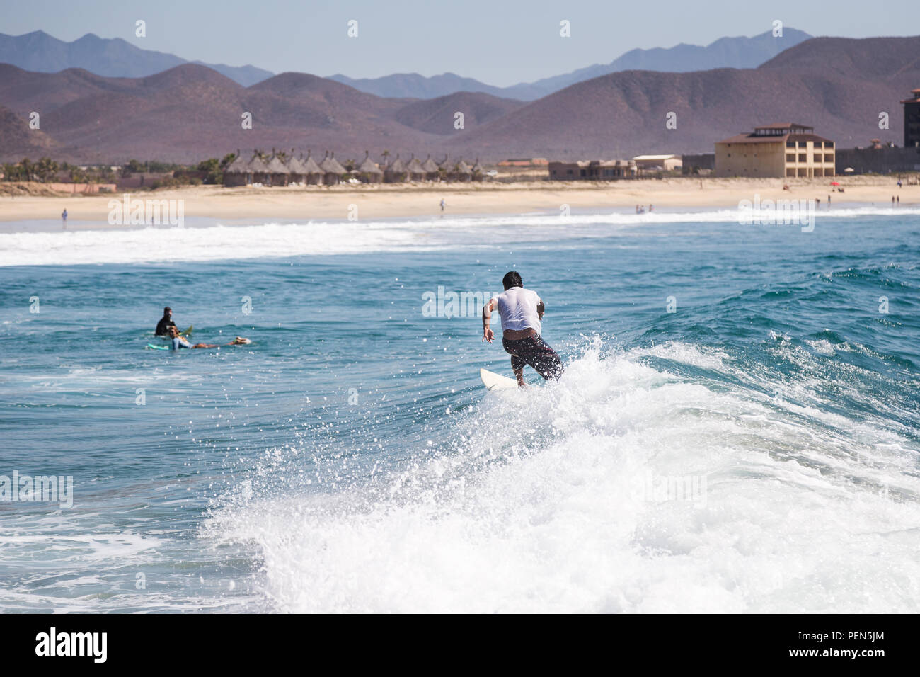 Surfer montando una onda con la playa en el fondo. Foto de stock