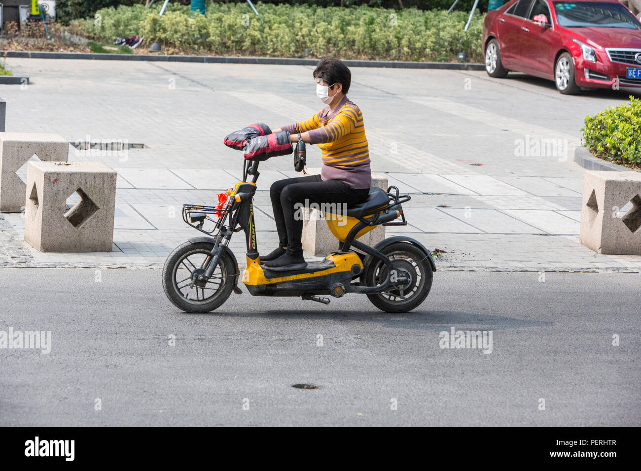 Suzhou, Jiangsu, China. Mujer con máscara respiratoria montando una motocicleta eléctrica. Foto de stock