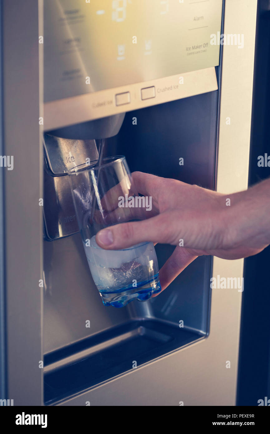Hombre mano está vertiendo agua fría y cubitos de hielo del dispensador de  la nevera en casa Fotografía de stock - Alamy