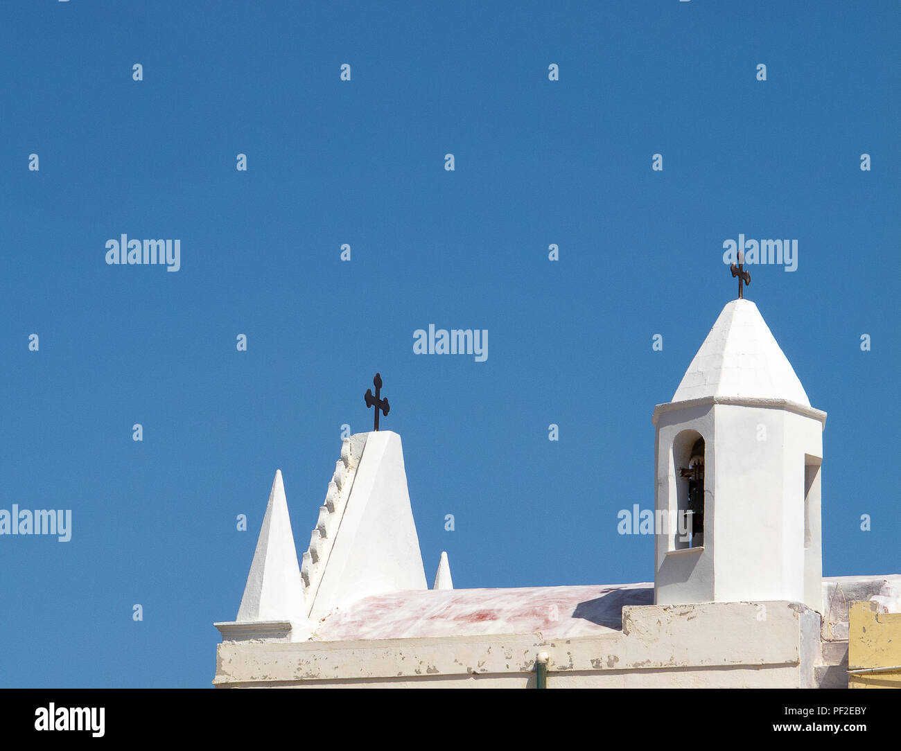 Calabria (Italia): techo y campanario de una pequeña iglesia blanca, con el azul del cielo despejado en el fondo, en un día soleado de verano Foto de stock