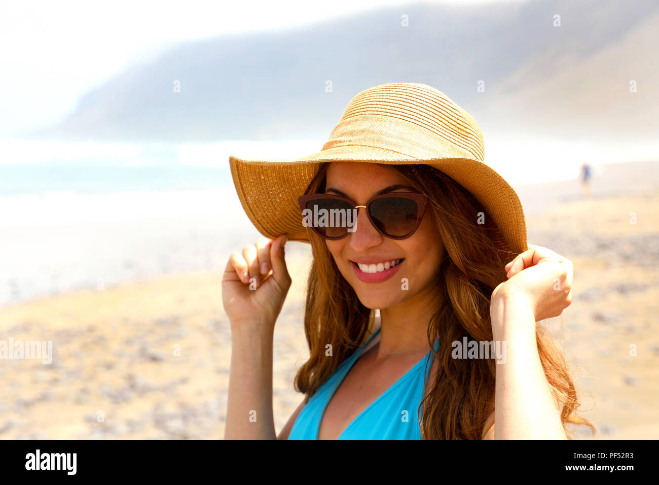 Hermosa joven en la playa con unas gafas de sol y sombrero de paja  sonriendo ante la cámara. Chica del viajero en sus vacaciones de verano en  las Islas Canarias. Vintage fi