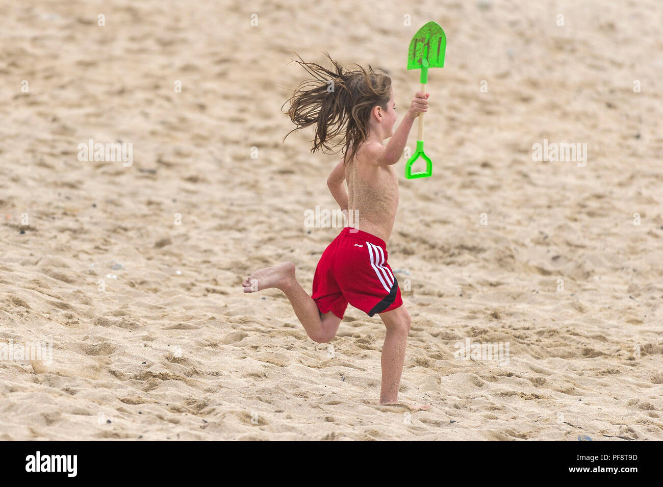 Un chico con el pelo largo corriendo por una duna de arena en la playa Fistral en Cornwall. Foto de stock