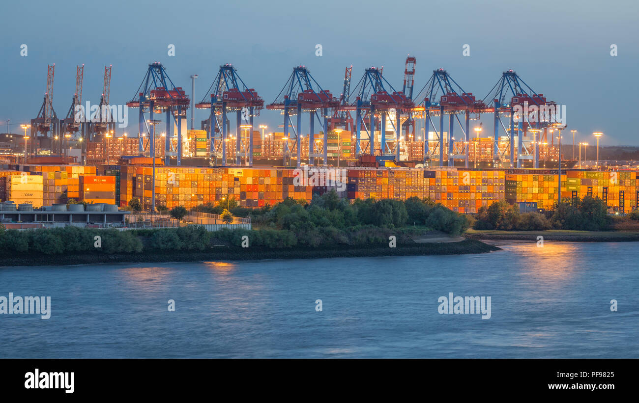Encendida en terminal de contenedores con grúas de carga sobre el río Elba, al anochecer, el puerto de Hamburgo, Hamburgo, Alemania. Foto de stock