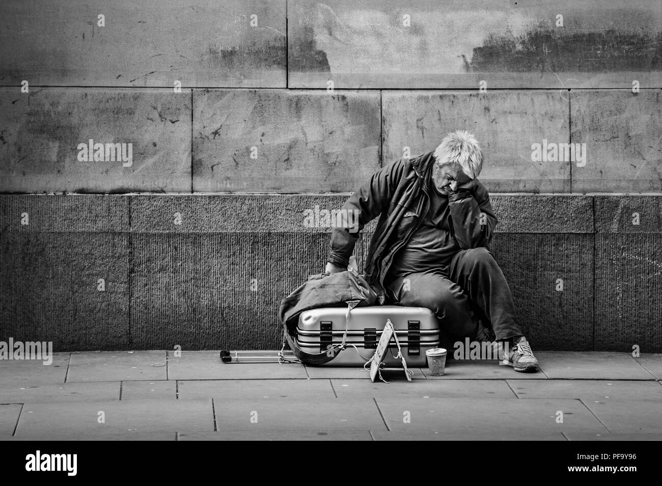 Hombre sin hogar con maleta durmiendo en las calles del centro de la ciudad de Manchester, Reino Unido Foto de stock
