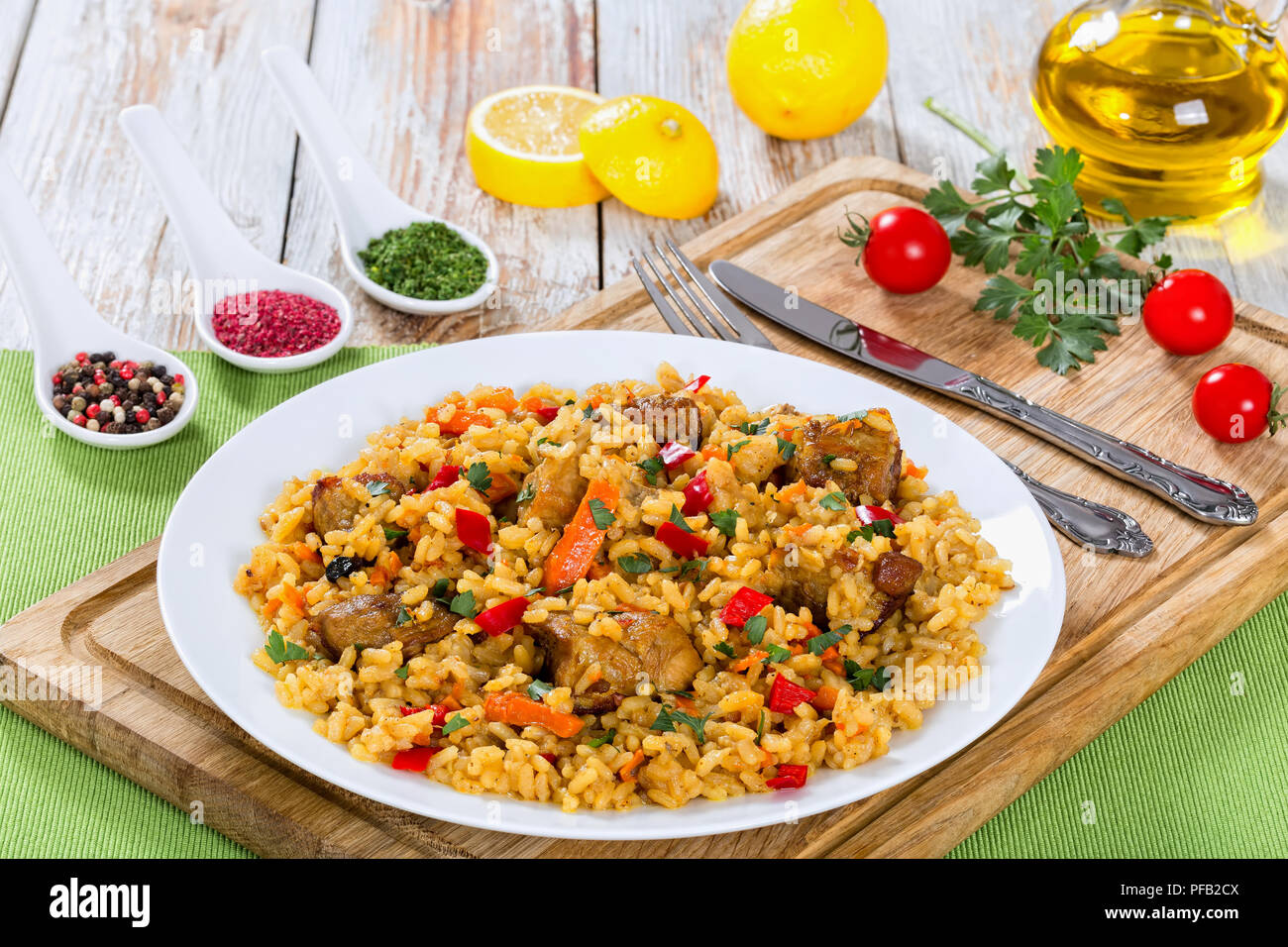 Sabrosa paella con carne, pimienta, hortalizas y especias en un plato sobre la tabla de cortar, la rodaja de limón, especias y tomates cherry sobre antecedentes, vista desde ab Foto de stock