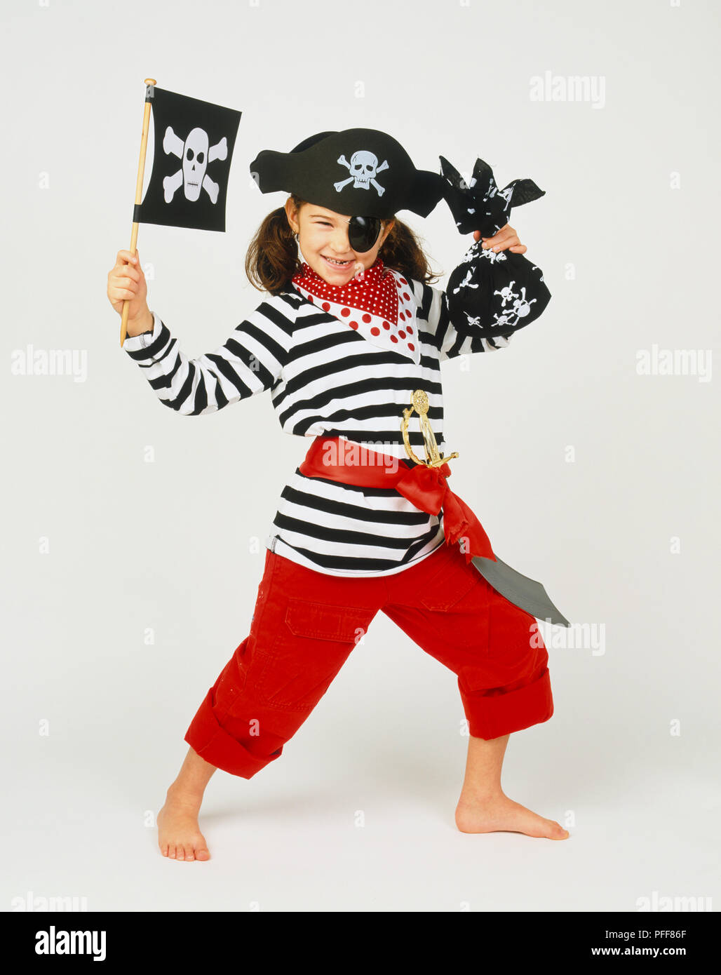 Chica sonriente con brown ponytails en pirate's outfit, sosteniendo la  bandera en una mano, saco negro en otros, vestidos de rojo, pantalón negro- blanco Camiseta de rayas creemos, bufanda punteado rojo-blanco, espada  agachada