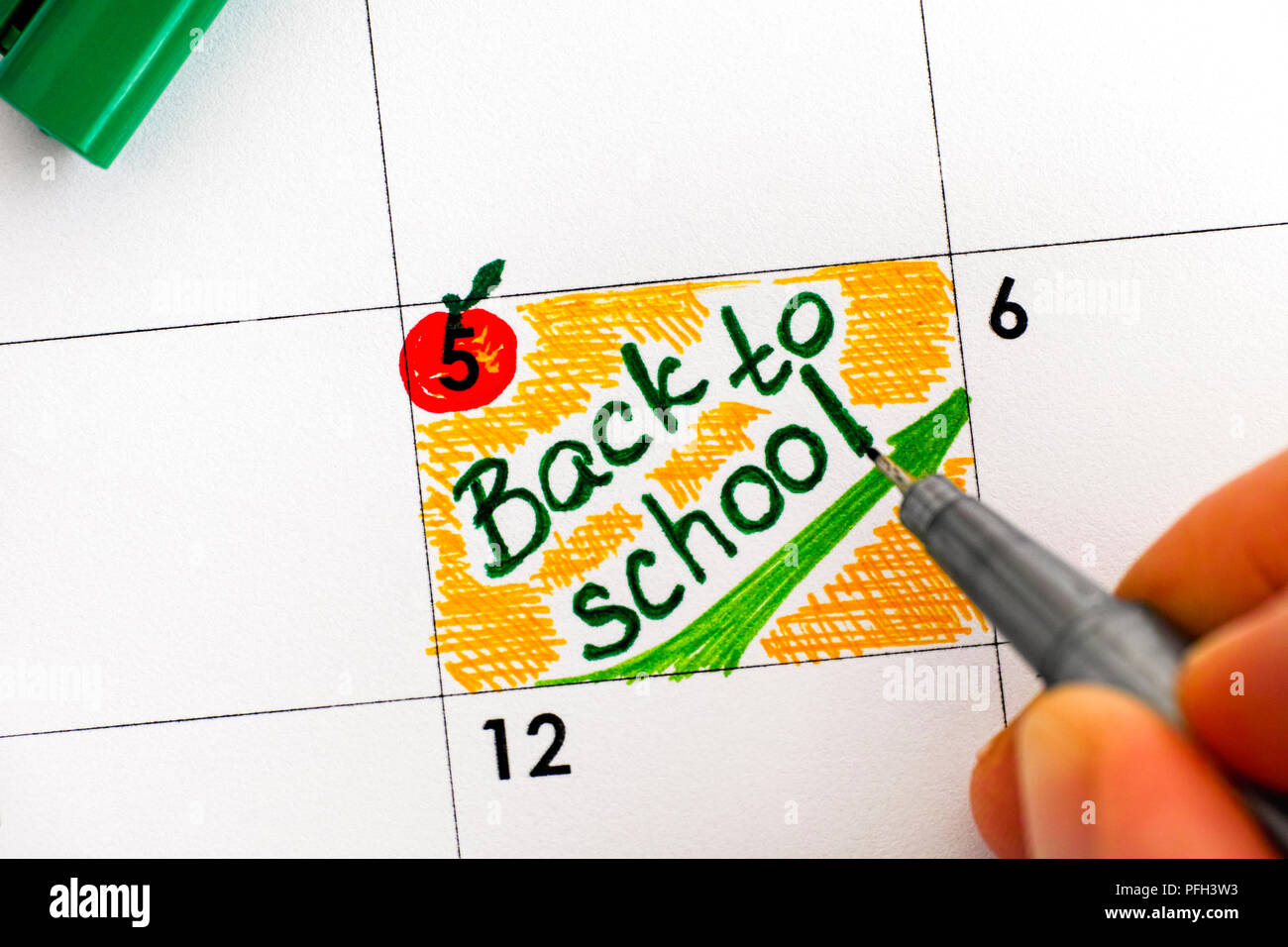 Mujer los dedos con lápiz verde escrito recordatorio volver a la escuela en el calendario. Close-up. Foto de stock