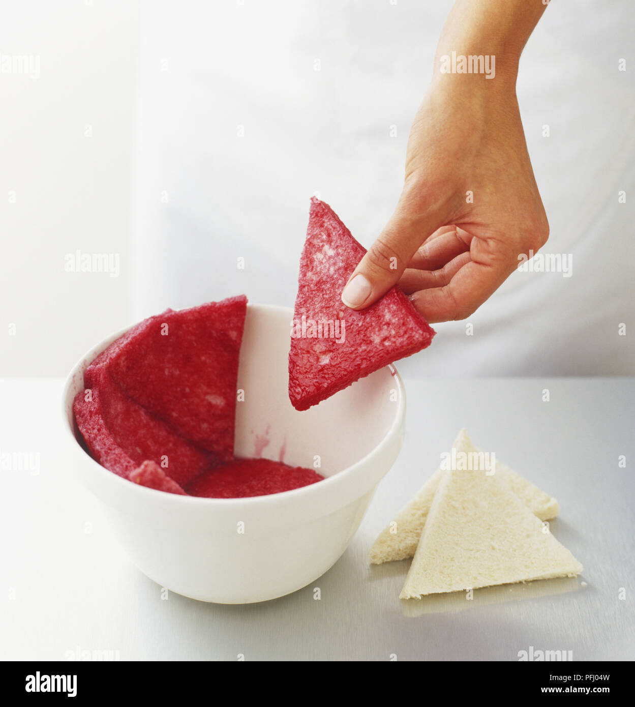 Revestimiento interior de un recipiente con triángulos de pan blanco empapado en jugo de frutas Foto de stock