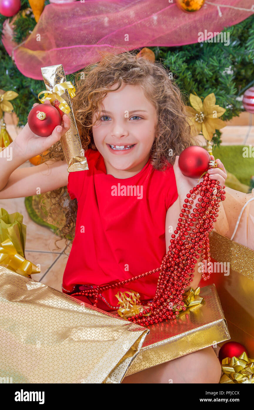 Cerca de chica sonriente blusa roja y sosteniendo una bola de Navidad,  decoración y regalo en sus manos, con un árbol de Navidad detrás, concepto  de navidad Fotografía de stock - Alamy