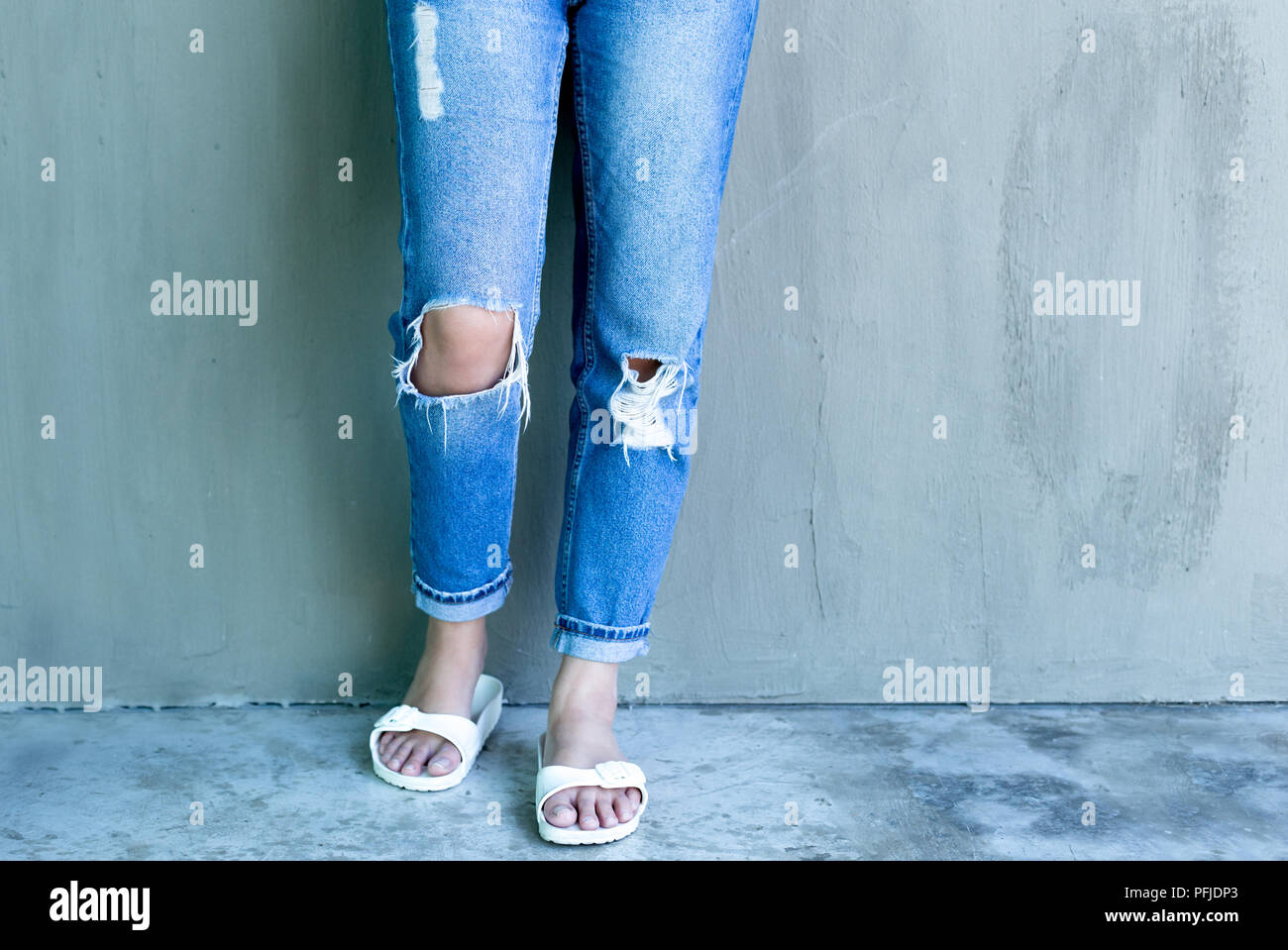 Mujer joven con moda jeans rajados y flip flop con muro de hormigón en  segundo plano Fotografía de stock - Alamy