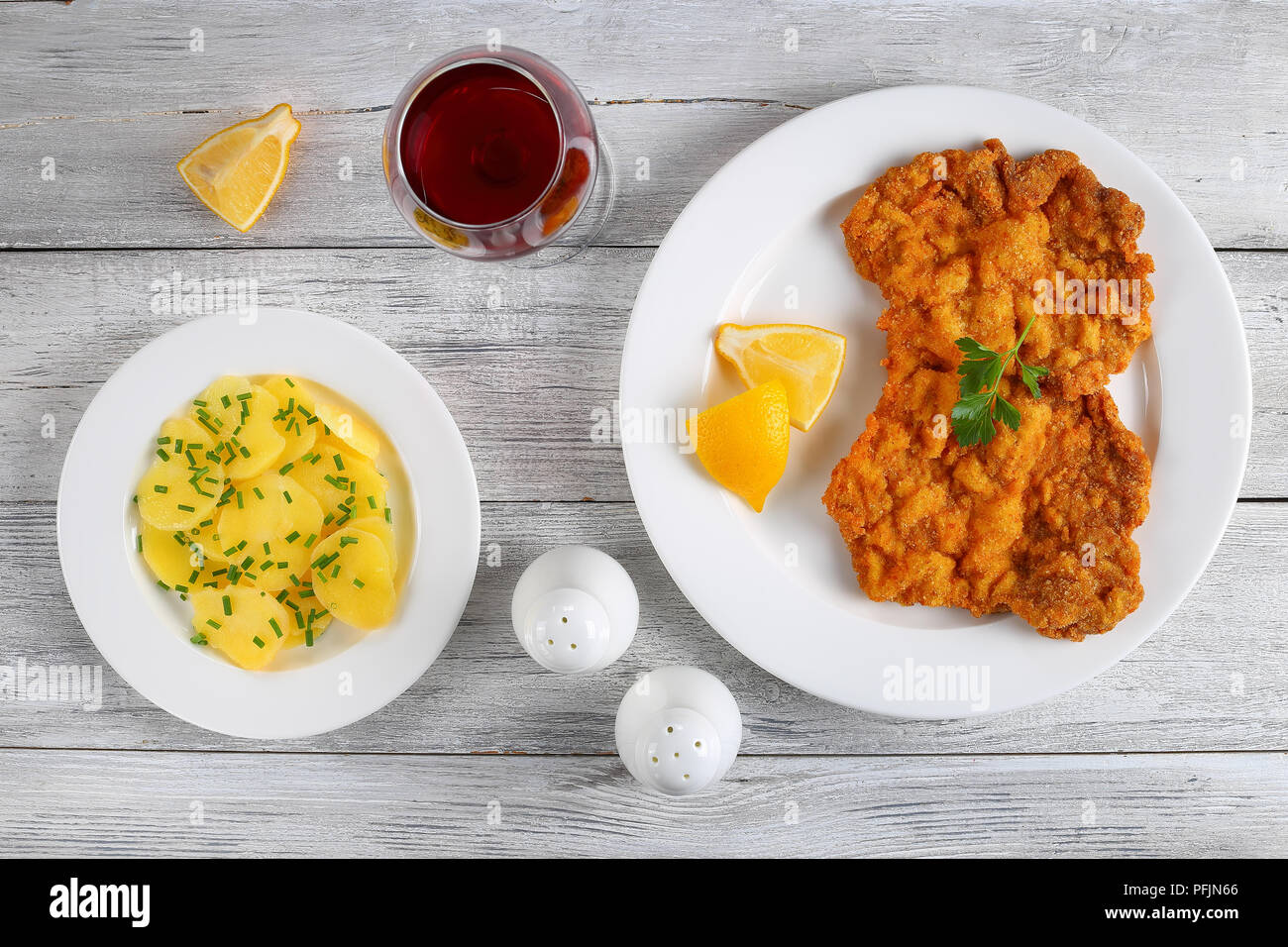 Deliciosas doradas Wiener Schnitzel clásico - o ternera empanada croquetas servido en la placa blanca con rodajas de limón sobre mesa de madera, ensalada de papas y gl Foto de stock