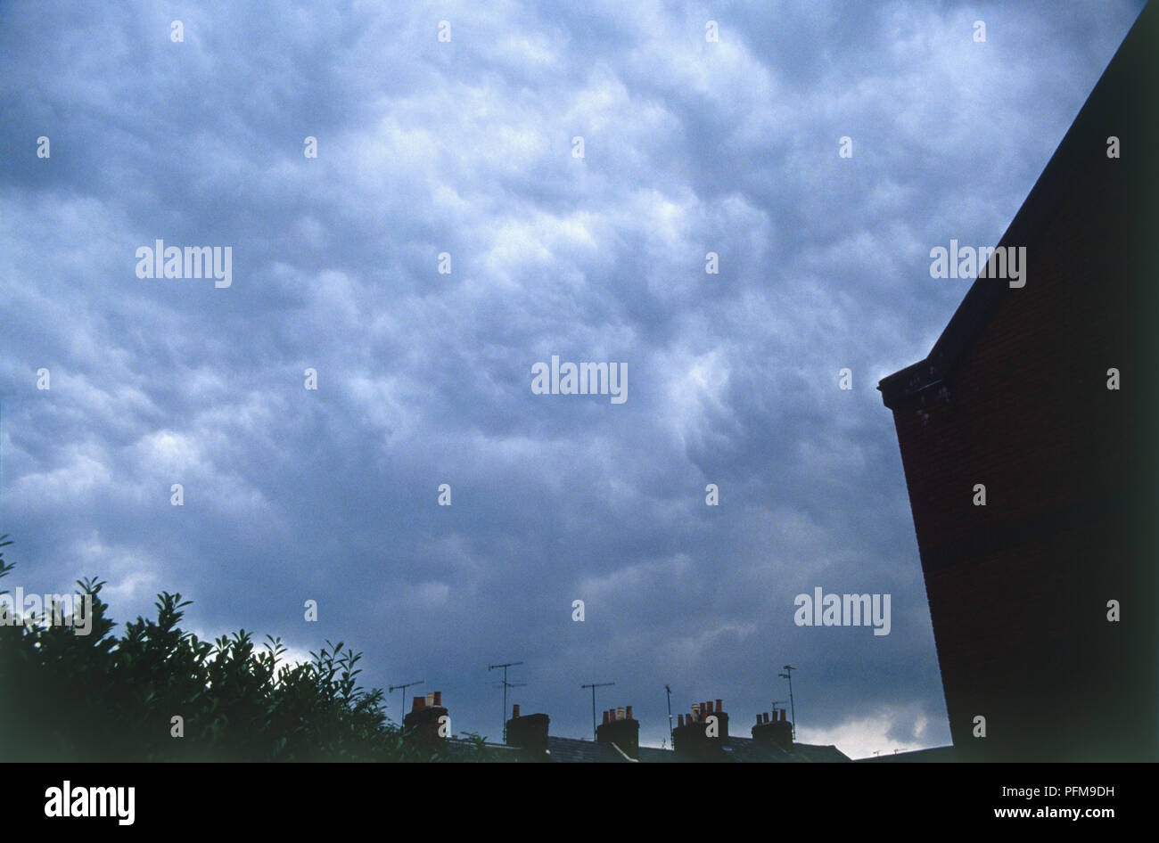 Altocúmulos nubes, acumulando en un oscurecimiento, cielo tormentoso por encima de tejados y chimeneas. Foto de stock