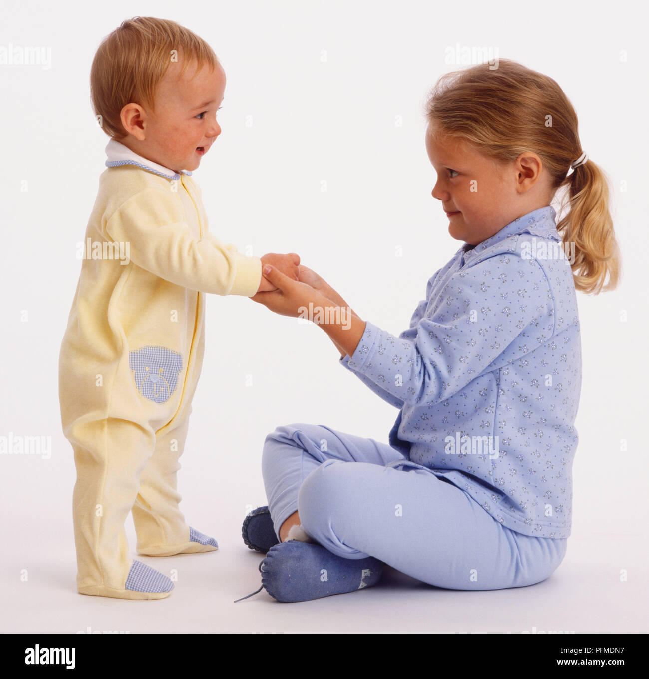 Muchacha en azul pijamas y Baby Boy en amarillo lista de reproducción manos Foto de stock