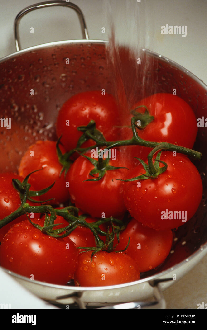 Close-up de vid roja los tomates en un colador después del enjuague bajo el agua. Las gotitas de agua reposan sobre los tomates y sus tallos. Foto de stock