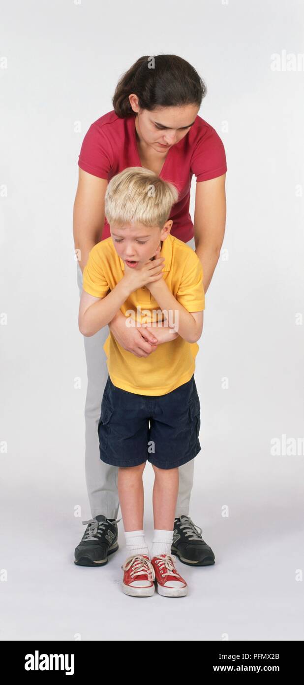 Niño sosteniendo su garganta, la mujer se situó detrás de él con sus brazos alrededor de él Foto de stock