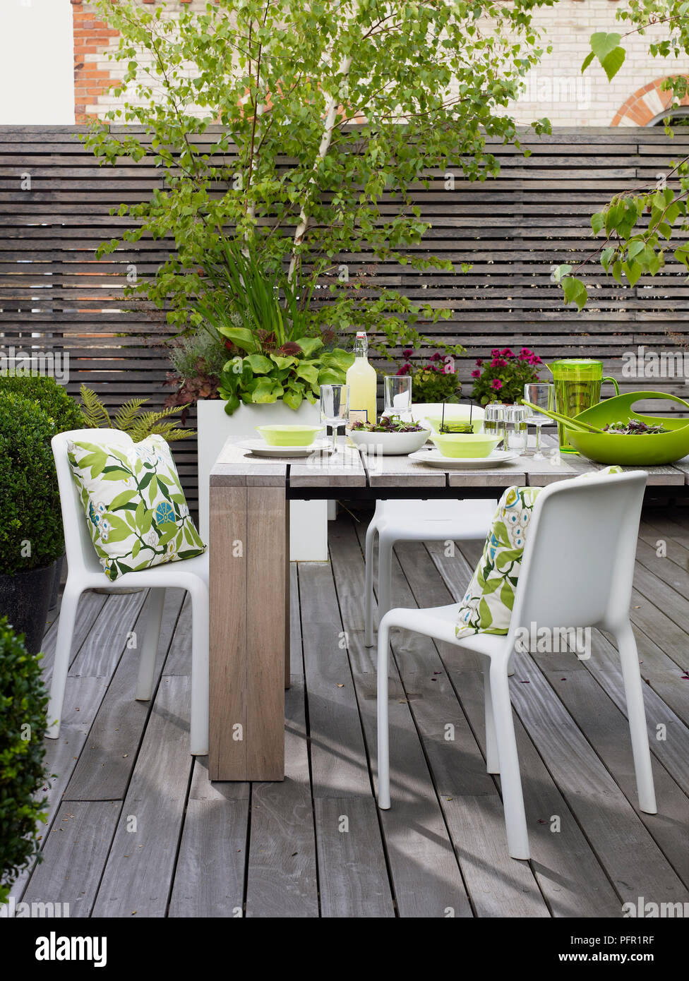 Mesa de madera para comer, visto desde el frente y patrón floral cojines en sillas  de plástico blancas sobre patio decorado Fotografía de stock - Alamy