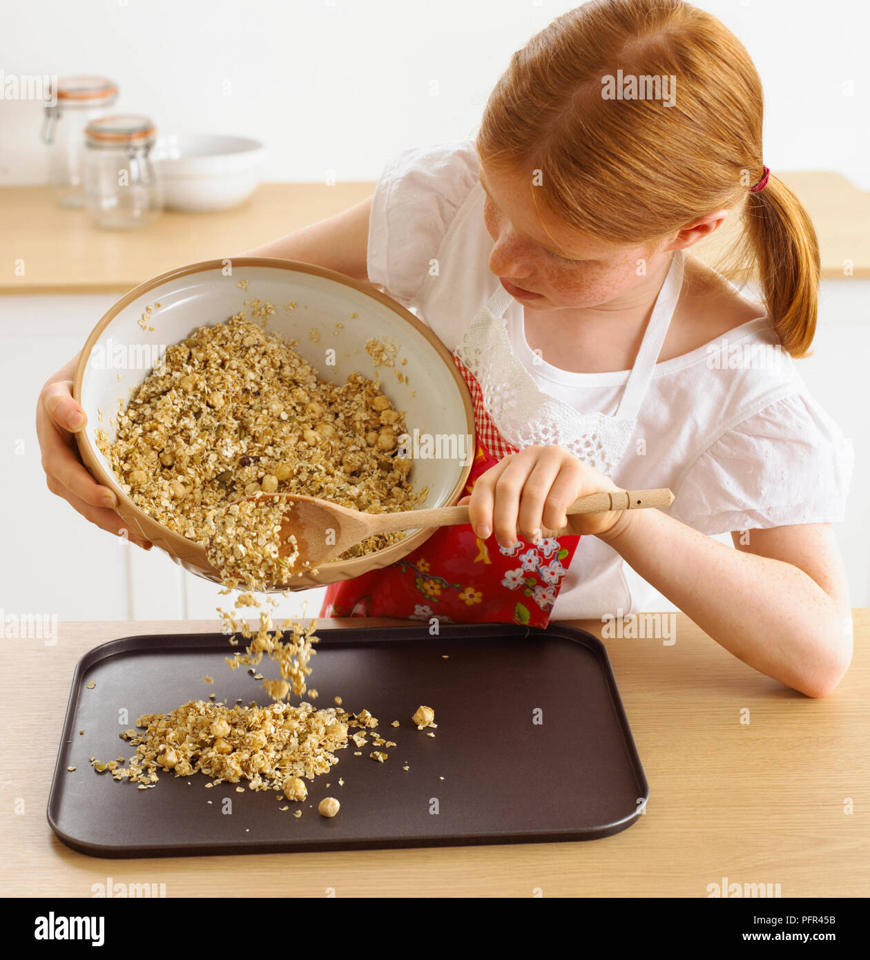 Chica colocando la mezcla de cereal en la bandeja para hornear, 9 años Foto de stock