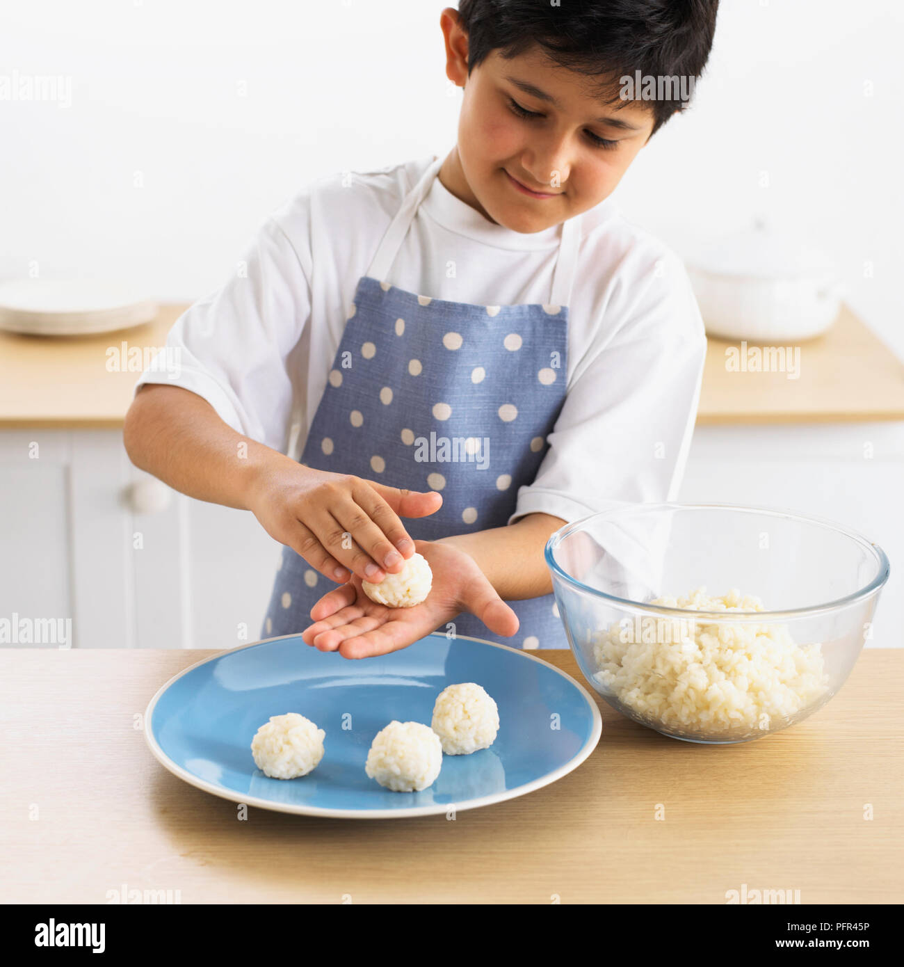 Muchacho Rodando la Bola de arroz entre las palmas de las manos, 9 años Foto de stock